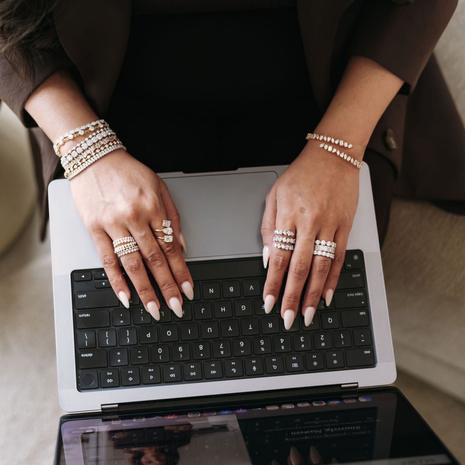 Close-up of hands wearing stacked diamond rings and bracelets while typing on a laptop.