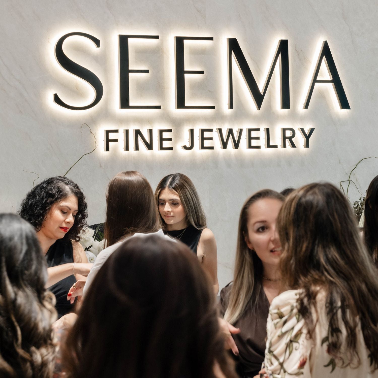 Guests gathered inside the Seema Fine Jewelry showroom beneath an illuminated wall sign during a private event.