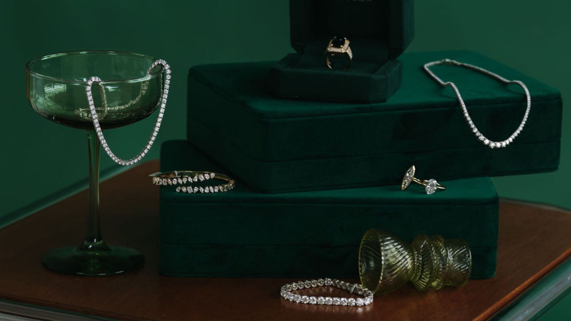 Green velvet display with a diamond tennis necklace, tennis bracelet, stud earrings, and a halo ring.