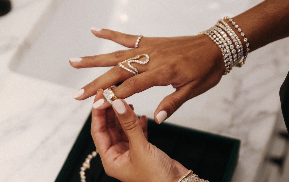 Slipping on a diamond ring at a marble vanity, wrists stacked with diamond bracelets