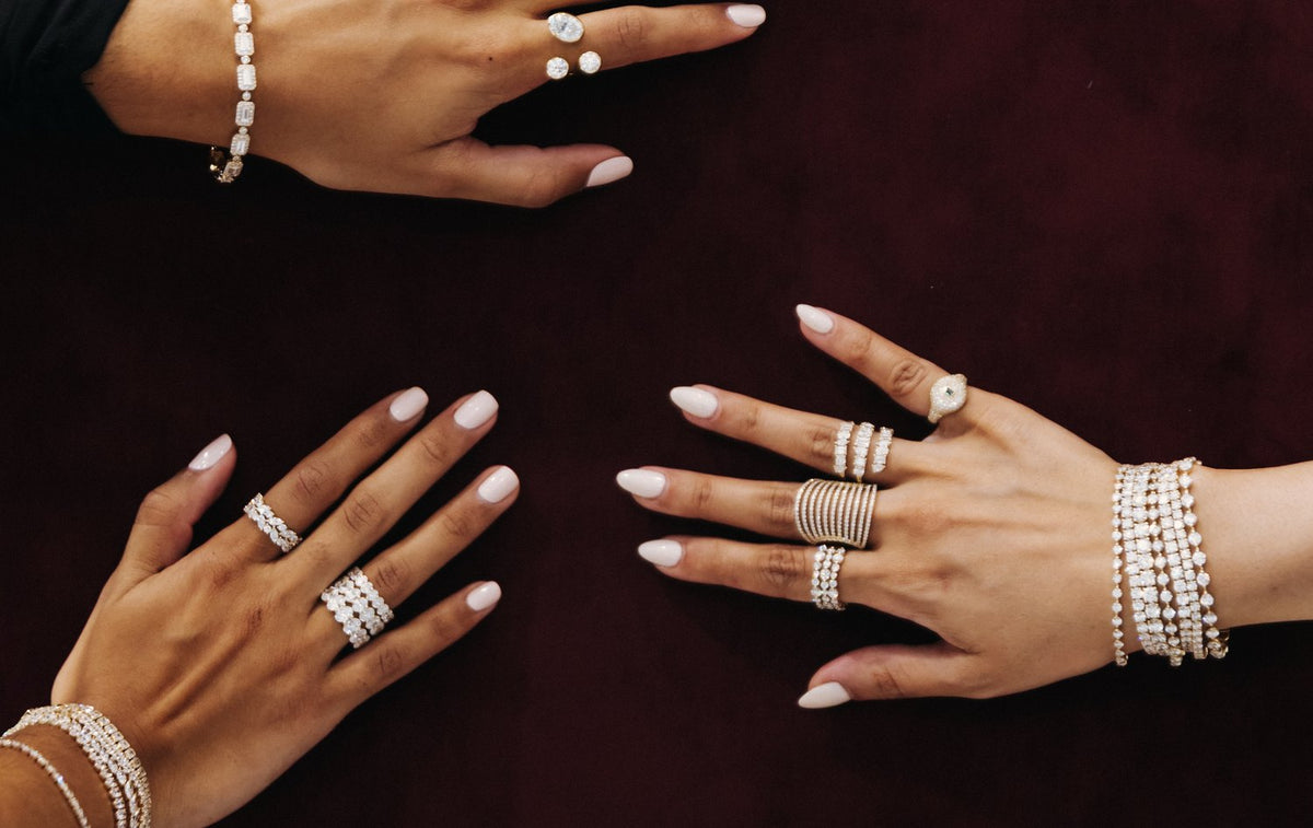 Four hands on dark velvet, wearing stacked diamond rings and bracelets
