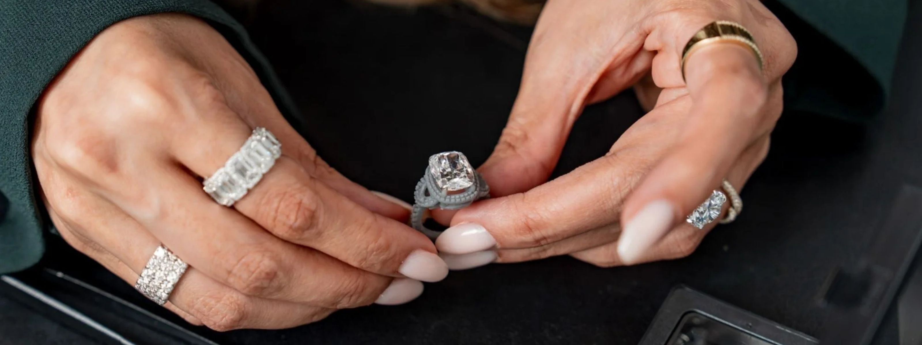 Two hands examining a cushion-cut diamond halo engagement ring over a dark velvet surface during a bridal consultation.