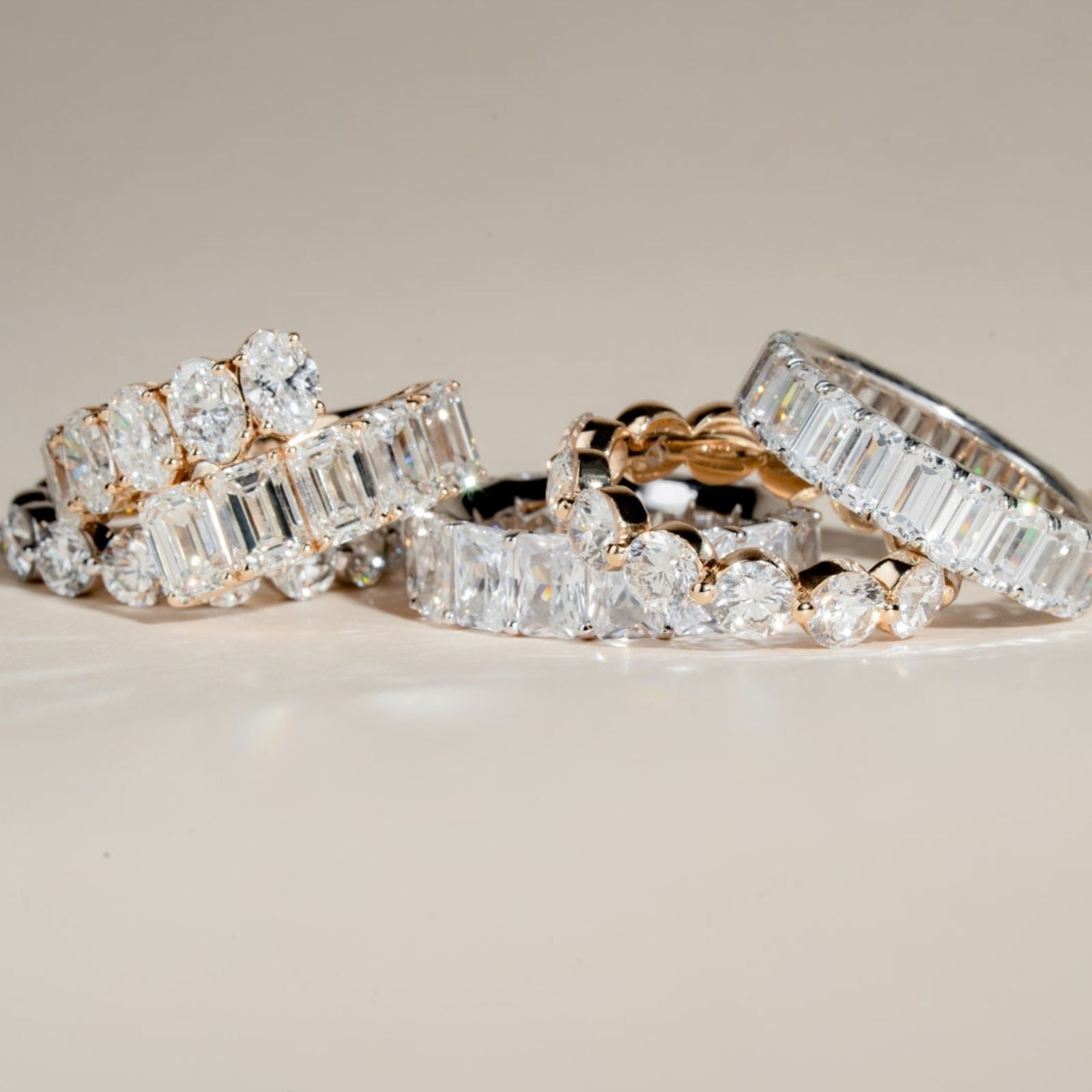 Seven diamond eternity bands in white and yellow gold arranged in a row including round, emerald-cut, baguette and marquise styles