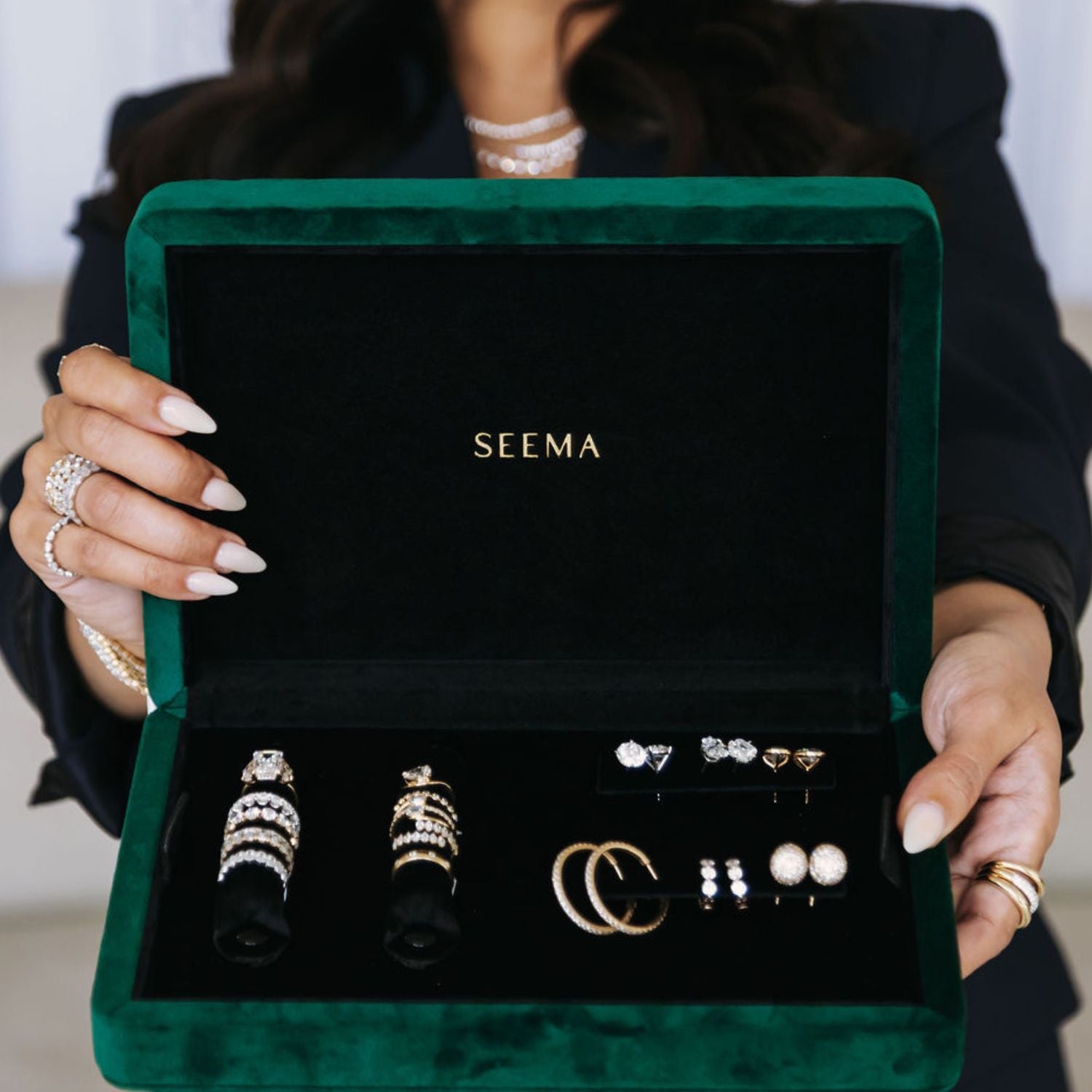 Jeweler presenting an open green velvet Seema jewelry box holding stacked diamond rings and earrings to a client.