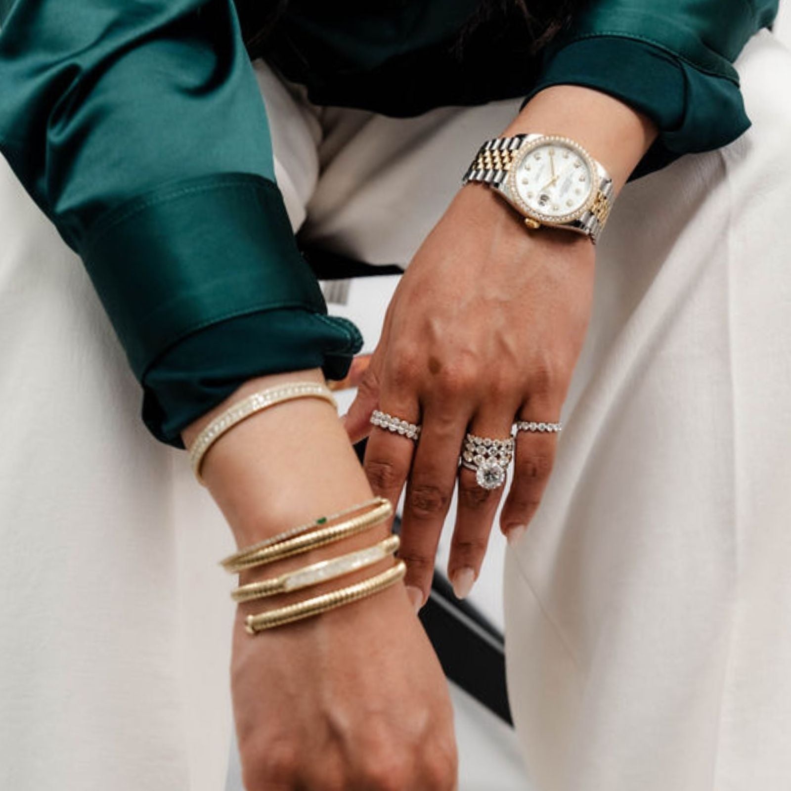 Hand wearing stacked gold bracelets and a two-tone watch with a diamond pavé ring.