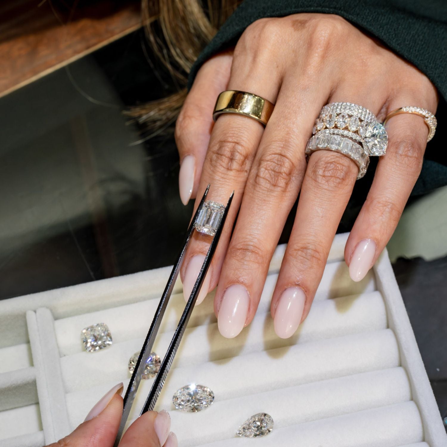 Jeweler holding an emerald-cut diamond with tweezers over a tray of loose diamonds including pear and cushion cuts.